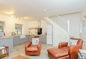 A modern kitchen with a central island, a dining area with leather chairs, and a staircase leading to an upper level.