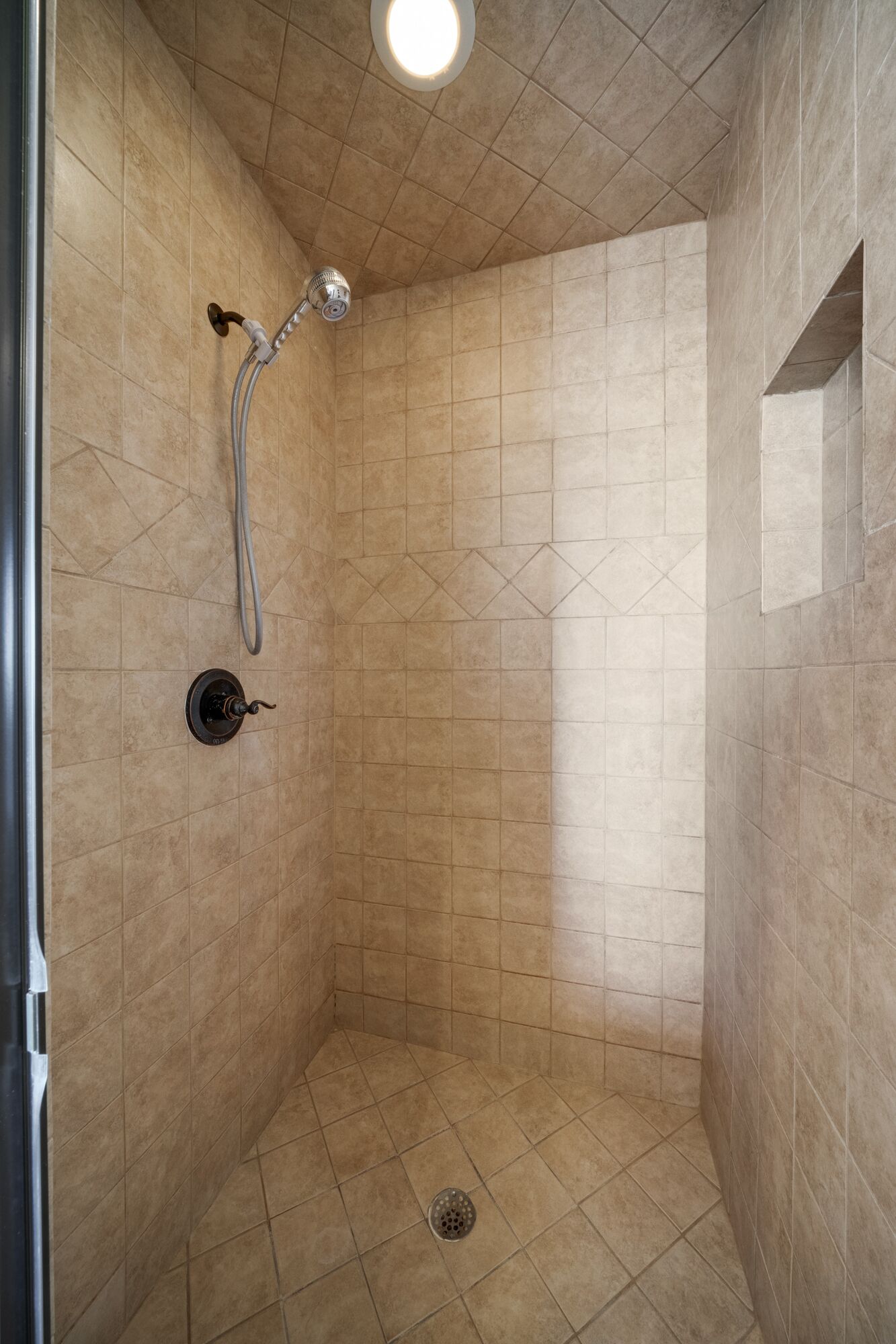 A small, tiled shower room with a handheld showerhead and a wall-mounted faucet.