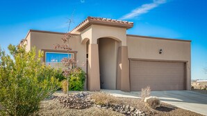A single-story house with a beige facade, a large garage door, and a small patio area with a rock garden. - *Tranquil Living in the City* (Las Cruces)
