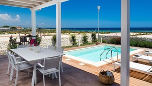 A covered outdoor area with a pool, white furniture, and a view of the sea. - Villa for 6 People in Sicily with private pool at the Sea (Reitani)