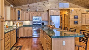 Eine Küche mit Holzausstattung, Granit-Arbeitsplatten, Edelstahlgeräten und einer zentralen Kochinsel mit Sitzgelegenheiten.