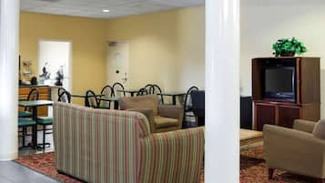 Un'accogliente hall d'hotel con un divano a righe, una televisione e un'area ristorazione con sedie e tavoli.
