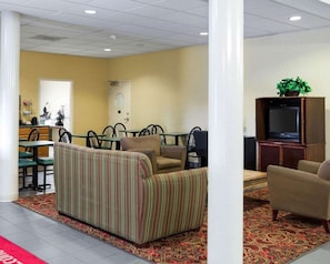 A hotel lobby with a striped sofa, a television, and a dining area with chairs and tables.