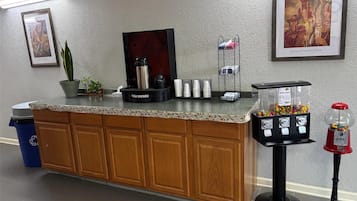 Un'area reception con un bancone, una macchina per caffè, un dispenser d'acqua, un cestino e un distributore automatico.