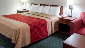 A hotel room with a bed, two bedside lamps, a telephone, a chair, and a painting on the wall.