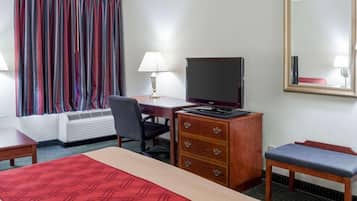 Una camera d'albergo con un letto, una scrivania con televisore, una sedia, un comodino e una finestra con tende.