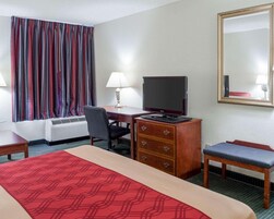 A hotel room with a bed, a desk with a television, a chair, a dresser, and a window with curtains.