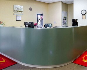 A hotel reception desk with a computer, a clock, and a framed certificate on the wall.