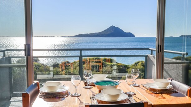 Une table dressée pour le dîner, avec vue sur la mer et une montagne à l’horizon.