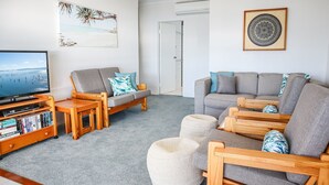 Un salon comprenant un canapé, des fauteuils, une table basse et un meuble pour la télévision, avec des livres.