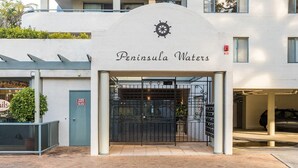 The entrance to Peninsula Waters with a nautical-themed sign, a gated entrance, and a fire exit door. - Peninsula Waters, 3/2-4 Soldiers Point Rd - Beautiful Air Conditioned Unit with Pool, Lift & WIFI (Soldiers Point)