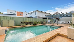 A rectangular swimming pool with a tiled deck, surrounded by a green fence and a pergola. - Peninsula Waters, 3/2-4 Soldiers Point Rd - Beautiful Air Conditioned Unit with Pool, Lift & WIFI (Soldiers Point)