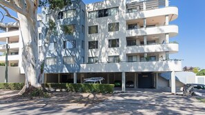 Um edifício residencial com vários andares, fachada plana, grandes janelas e área de estacionamento na frente.