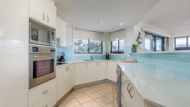 A modern kitchen with white cabinets, a built-in oven, a kettle, and a window providing natural light. - Peninsula Waters, 3/2-4 Soldiers Point Rd - Beautiful Air Conditioned Unit with Pool, Lift & WIFI (Soldiers Point)