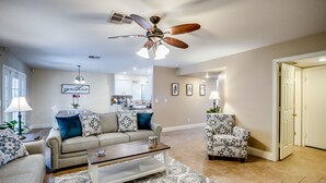 Un salon avec un ventilateur de plafond, un canapé, un fauteuil à motifs, une table basse et un tapis.