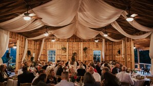 A large hall with wooden walls and ceiling, adorned with draped fabric. Tables are set with chairs, and people are seated.