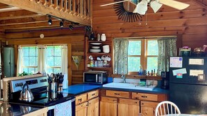A cabin-style kitchen with a stove, microwave, sink, and wooden cabinets.
