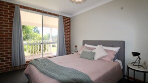 A bedroom with a large bed, a nightstand, a lamp, and a view of a balcony.