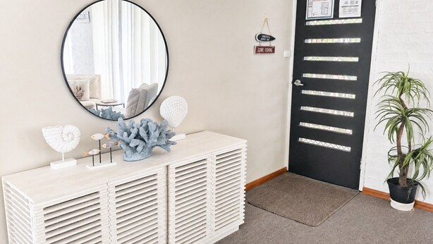A room with a round mirror, a white console table with decorative items, a black door with frosted glass panels, and a potted plant.