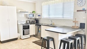 A compact kitchen with a stove, oven, dishwasher, and a small island with stools.
