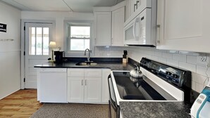 A modern kitchen with white cabinetry, a black countertop, a stainless steel sink, a stove, and a microwave. - Mountains to Sea | Pet Friendly + Steps to Beach! (Holly Ridge)