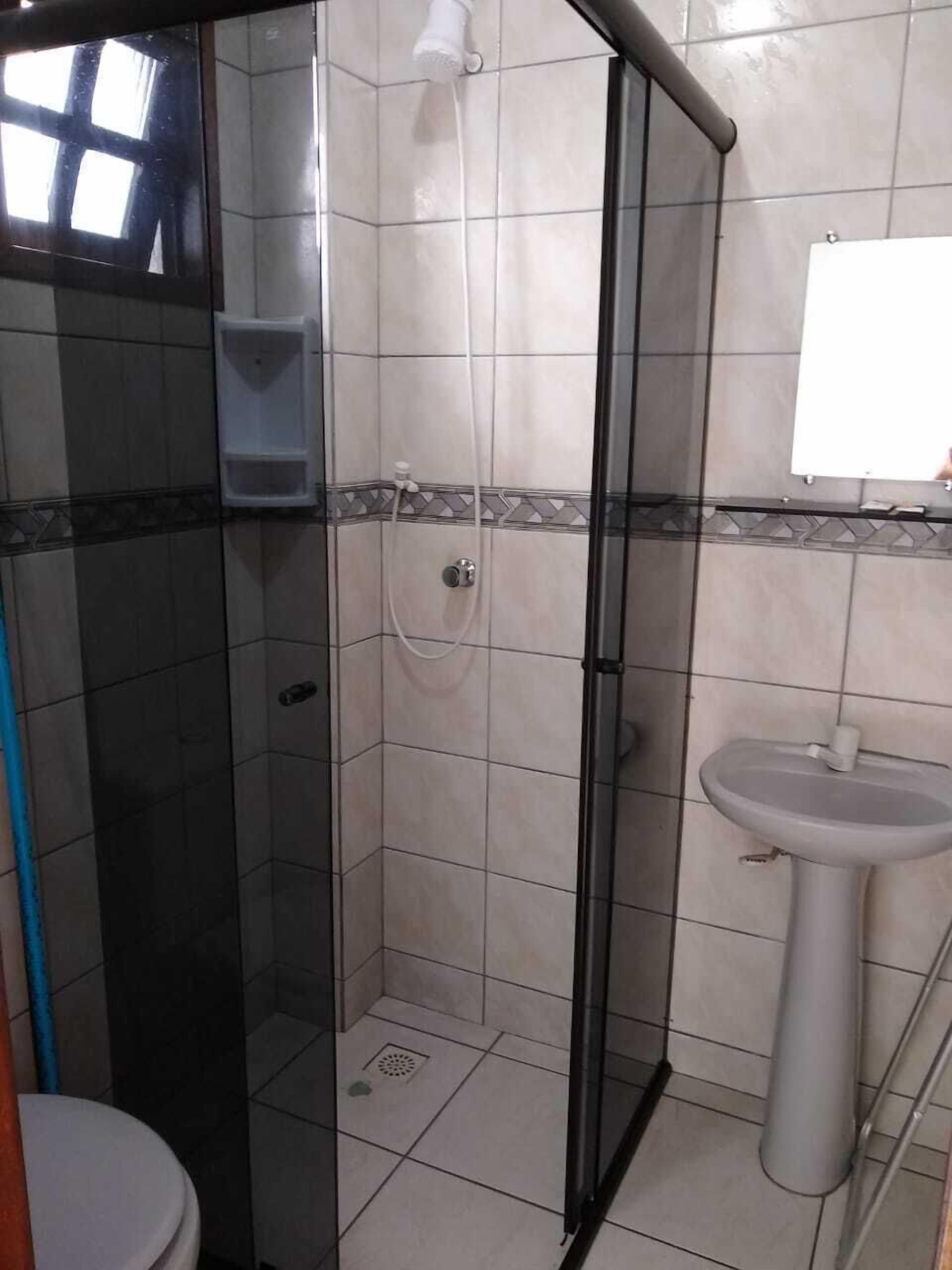 A bathroom with a glass-enclosed shower, a pedestal sink, and a toilet.