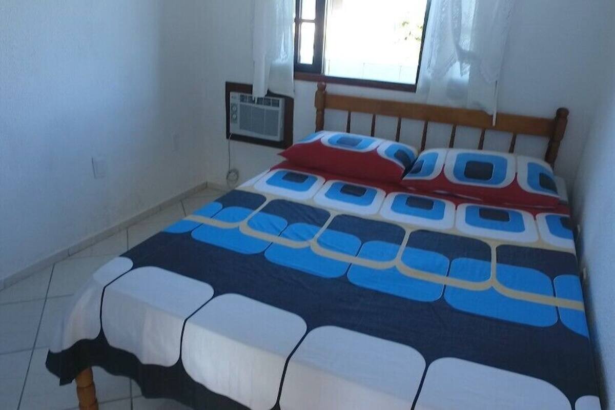 Ein Bett mit einem gemusterten Bettbezug, einem Holzkopfstück und einem Fenster mit Vorhängen.