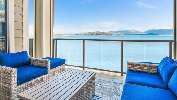 Un balcon doté de meubles en osier et offrant une vue sur un lac et des montagnes lointaines.