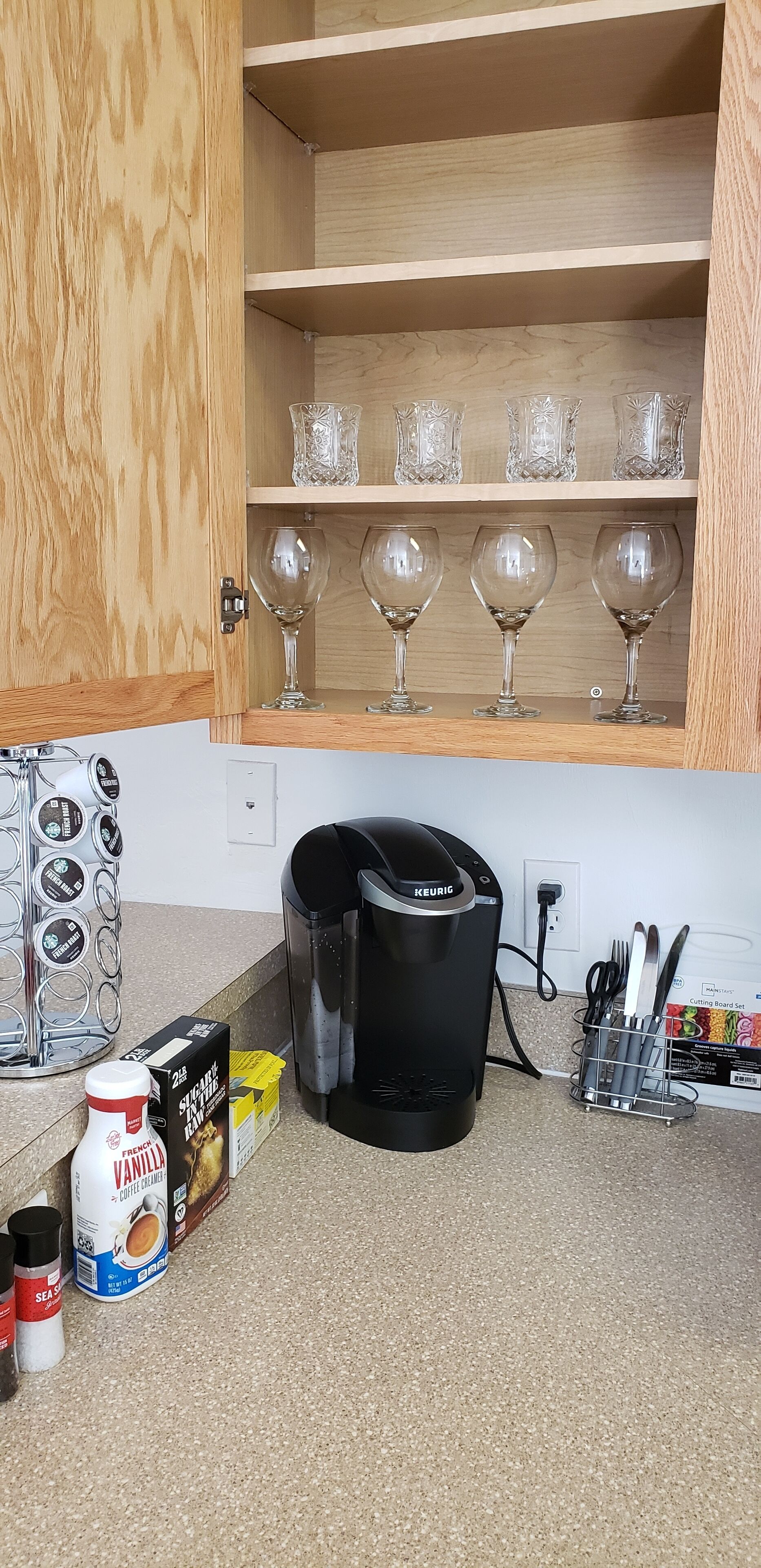 A kitchen with a coffee maker, a cabinet with wine glasses, and a coffee machine.