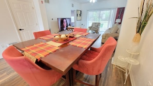 A dining area with a wooden table, red chairs, and a television in the background.