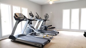 A fitness room with treadmills, large windows, and a ceiling fan.