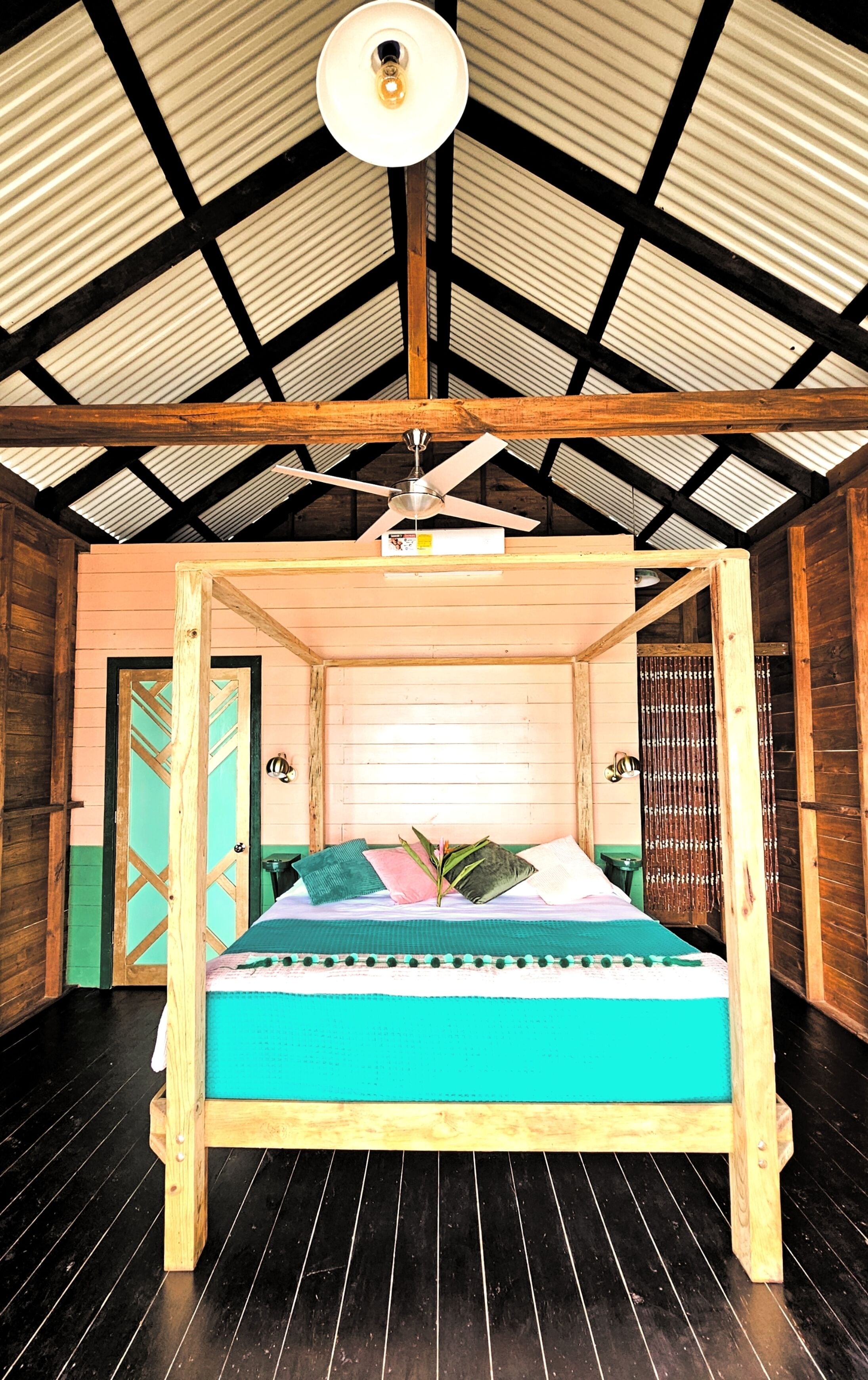 A wooden four-poster bed with a teal bedspread in a room with a high ceiling and wooden beams.