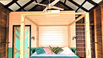 A wooden four-poster bed with a teal bedspread in a room with a high ceiling and wooden beams.