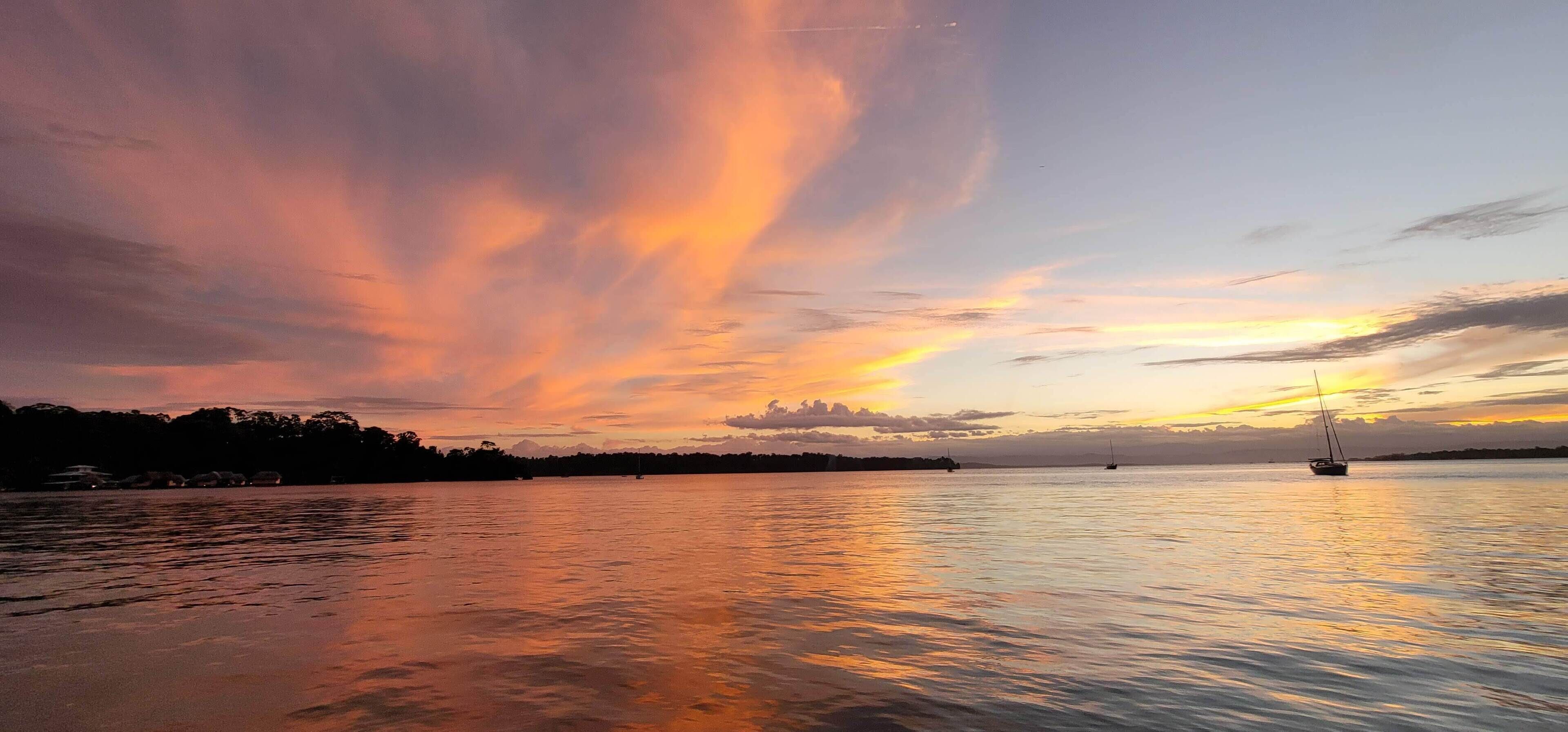 A sunset over a calm body of water with sailboats.