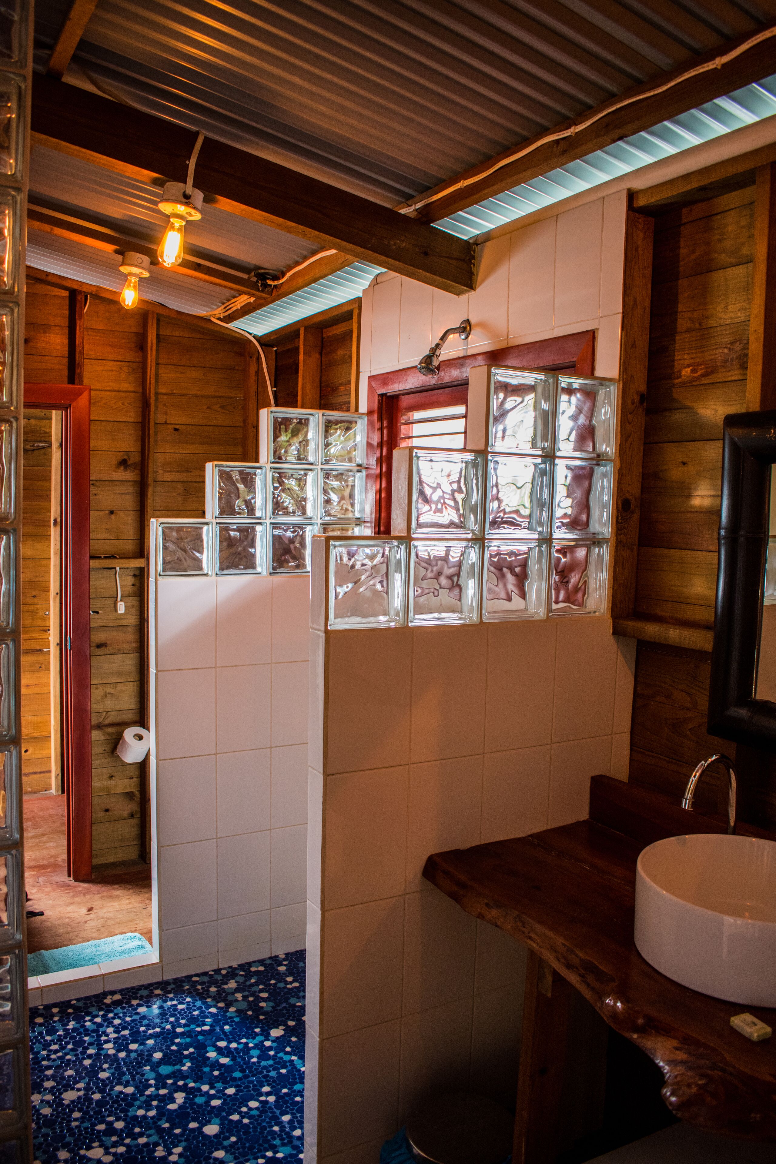 A rustic bathroom with a wooden vanity, a white sink, and a blue-tiled floor.