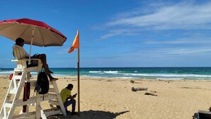 A lifeguard tower with a red umbrella and a flag on a sandy beach with the ocean in the background.