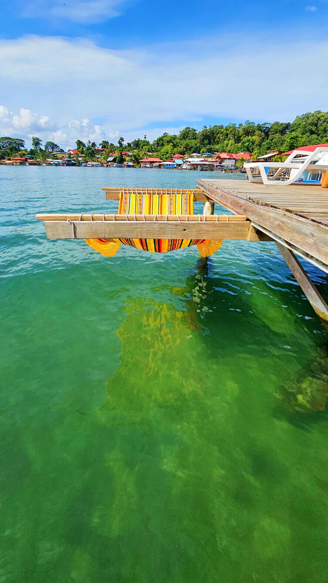 A wooden pier extending into clear turquoise water with a colorful striped awning.
