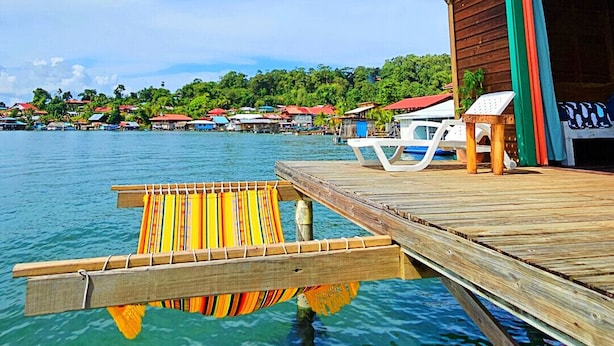 A wooden dock extending into clear blue water with a wooden building and a covered area with a green door.
