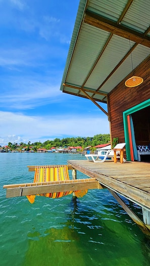 A wooden dock extending into clear blue water with a wooden building and a covered area with a green door. - The Sea Monkey (Bastimentos)