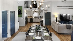 A dining area with a long wooden table set for six, a chandelier, and a kitchen in the background. - Georgetown Lake Retreat (Anaconda)