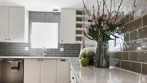 A kitchen with white cabinets, a tiled backsplash, a marble countertop, and a decorative vase with flowers. - Georgetown Lake Retreat (Anaconda)