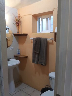 A compact bathroom with a sink, toilet, and towel rack, featuring a mirror and a small window.