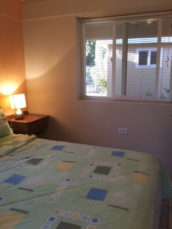 Un dormitorio con cama, mesita de noche, lámpara y ventana con persianas.