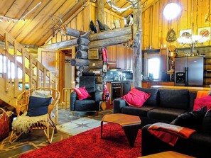 Ein rustikales Interieur mit Kamin aus Stein, Holzbalken, einem Essbereich und einer Küche mit modernen Geräten.
