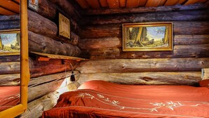 Hirsihuone, jossa on kaksi sänkyä, puuseinät ja maalaus, jossa on kuvattuna metsämaisema.