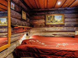 Una habitación de cabaña de troncos con dos camas, paredes de madera y cuadros enmarcados.