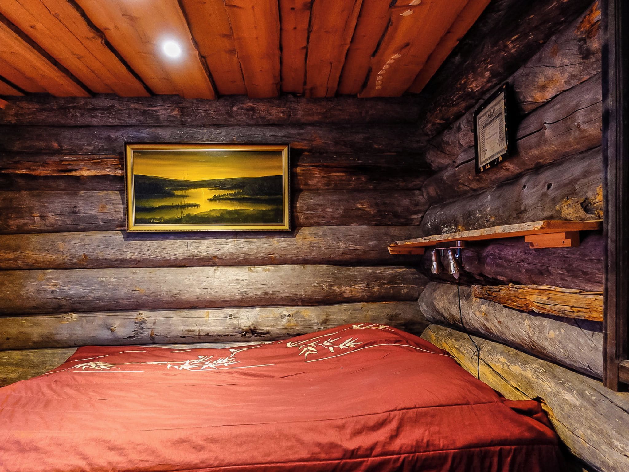 A log cabin interior with a bed, a painting, and a shelf with items.