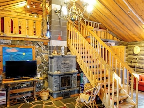 A cozy cabin interior with a stone fireplace, wooden staircase, and a television on a wooden stand.