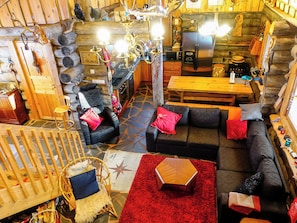 Interior acogedor de una cabaña de madera con sala de estar que incluye un sofá, una mesa de comedor y una chimenea.