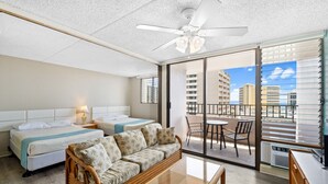 Une chambre d’hôtel avec deux lits, un canapé, un balcon avec une table et des chaises, et une vue sur la ville.